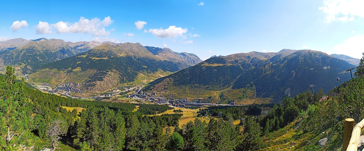 A mountainous landscape with a town nestled in a valley, surrounded by dense forests and distant peaks.