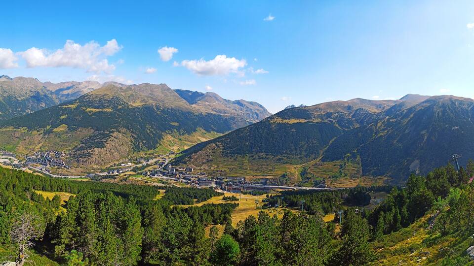 A mountainous landscape with a town nestled in a valley, surrounded by dense forests and distant peaks.