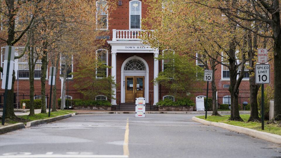 A brick building with a white entrance, trees lining the street, and a speed limit sign of 10.