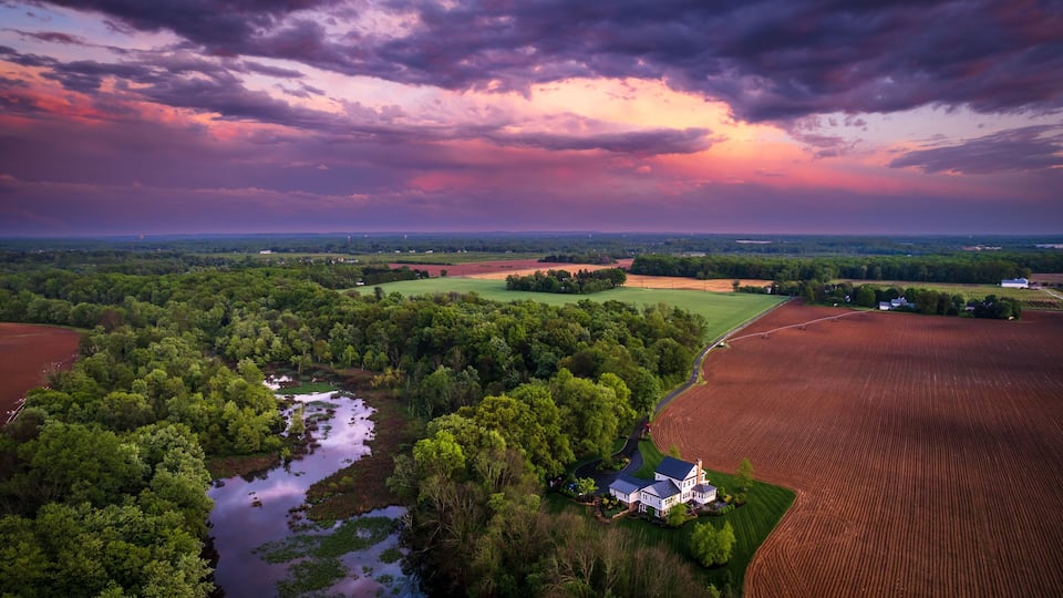A rural landscape with a river, fields, and a farmhouse.