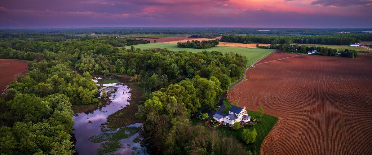 A rural landscape with a river, fields, and a farmhouse.