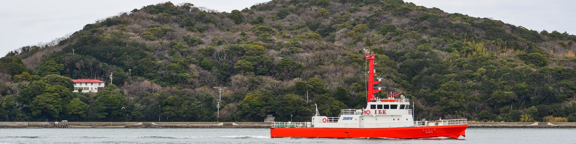 A red and white boat on calm water with a forested hill in the background.