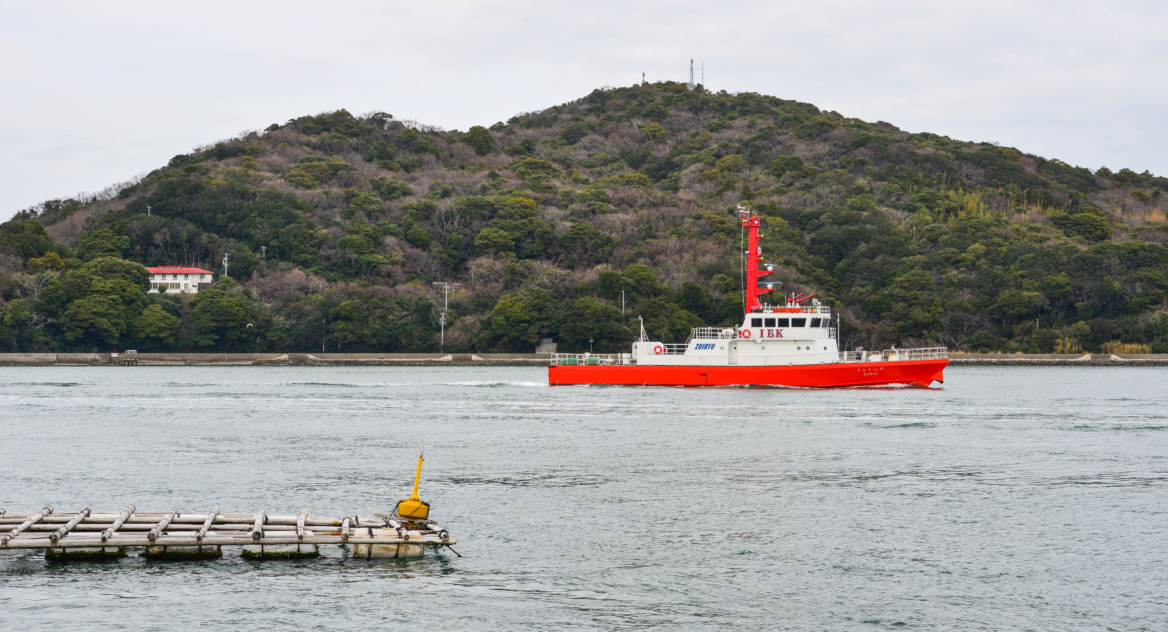 A red and white boat on calm water with a forested hill in the background.