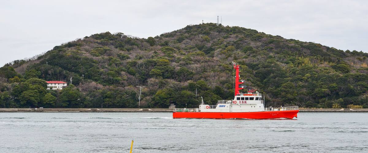 A red and white boat on calm water with a forested hill in the background.
