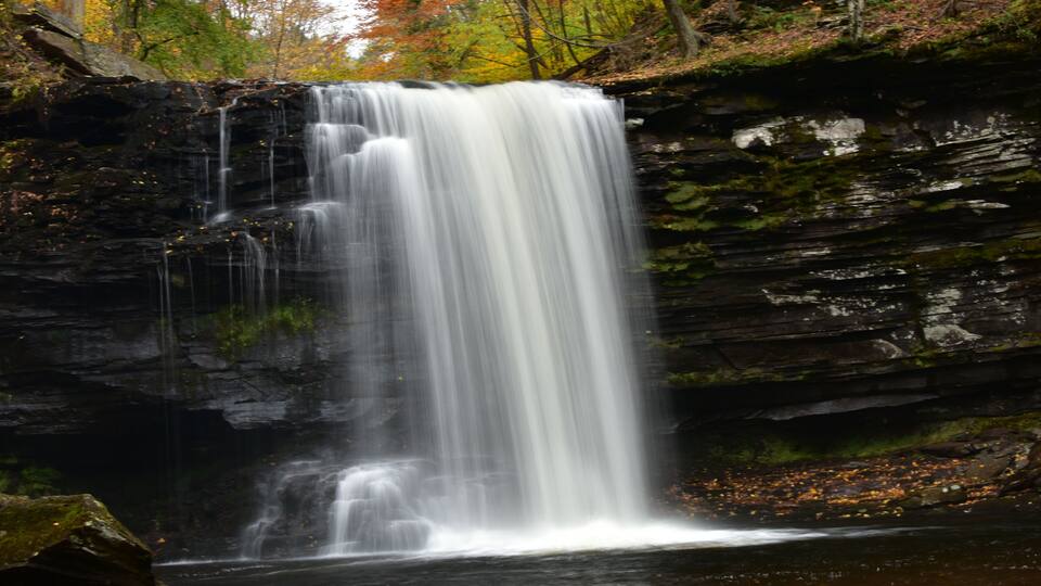A waterfall cascading down a rocky cliff surrounded by autumn foliage.