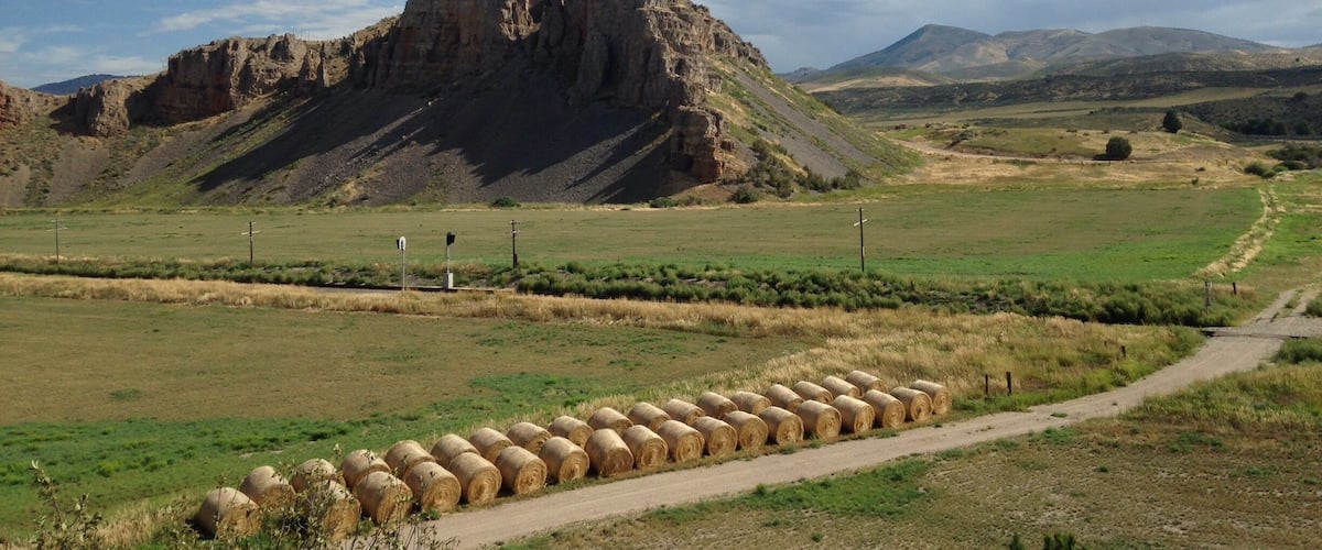 A rural landscape with a prominent rocky hill, hay bales, and a dirt road.