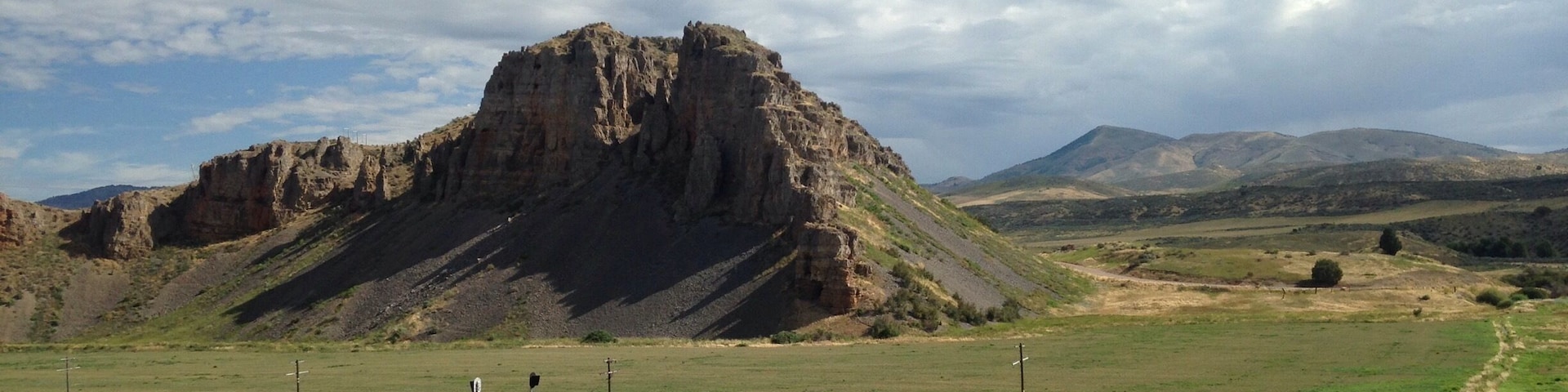 A rural landscape with a prominent rocky hill, hay bales, and a dirt road.