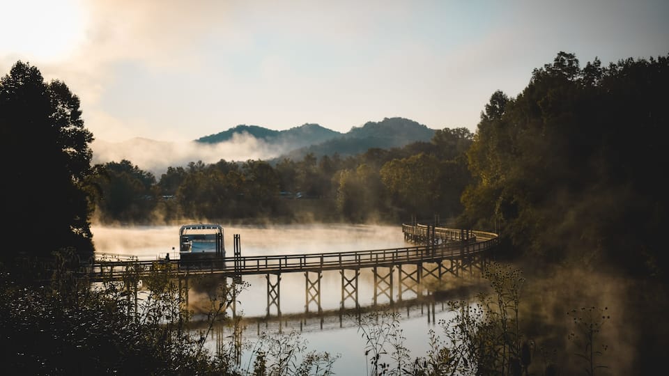 A bridge over a misty lake with mountains in the background.
