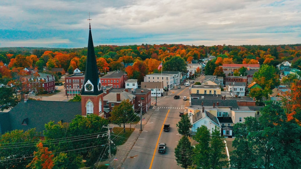 A town with a prominent church steeple, autumn-colored trees, and a mix of historic and modern buildings.