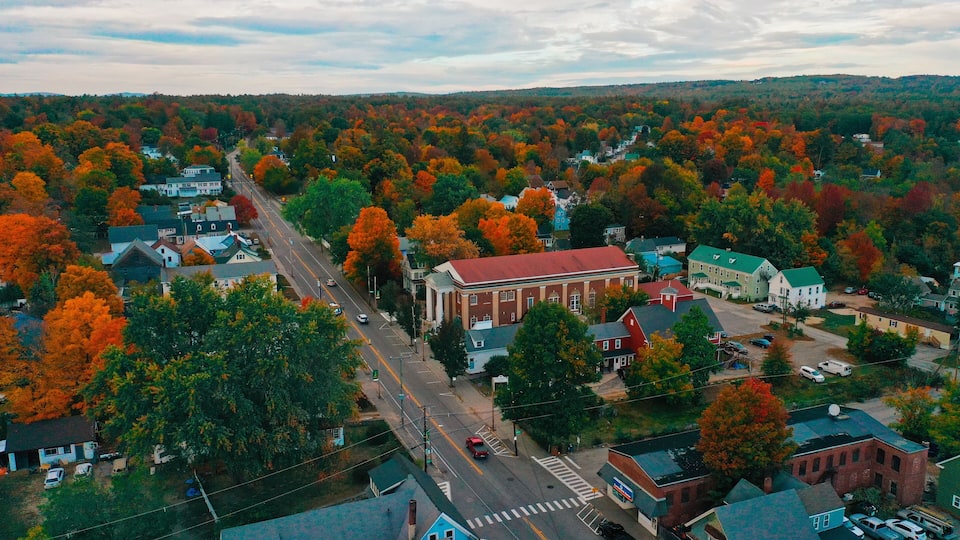 An aerial view of a town with autumn-colored trees, a main road, and various buildings.
