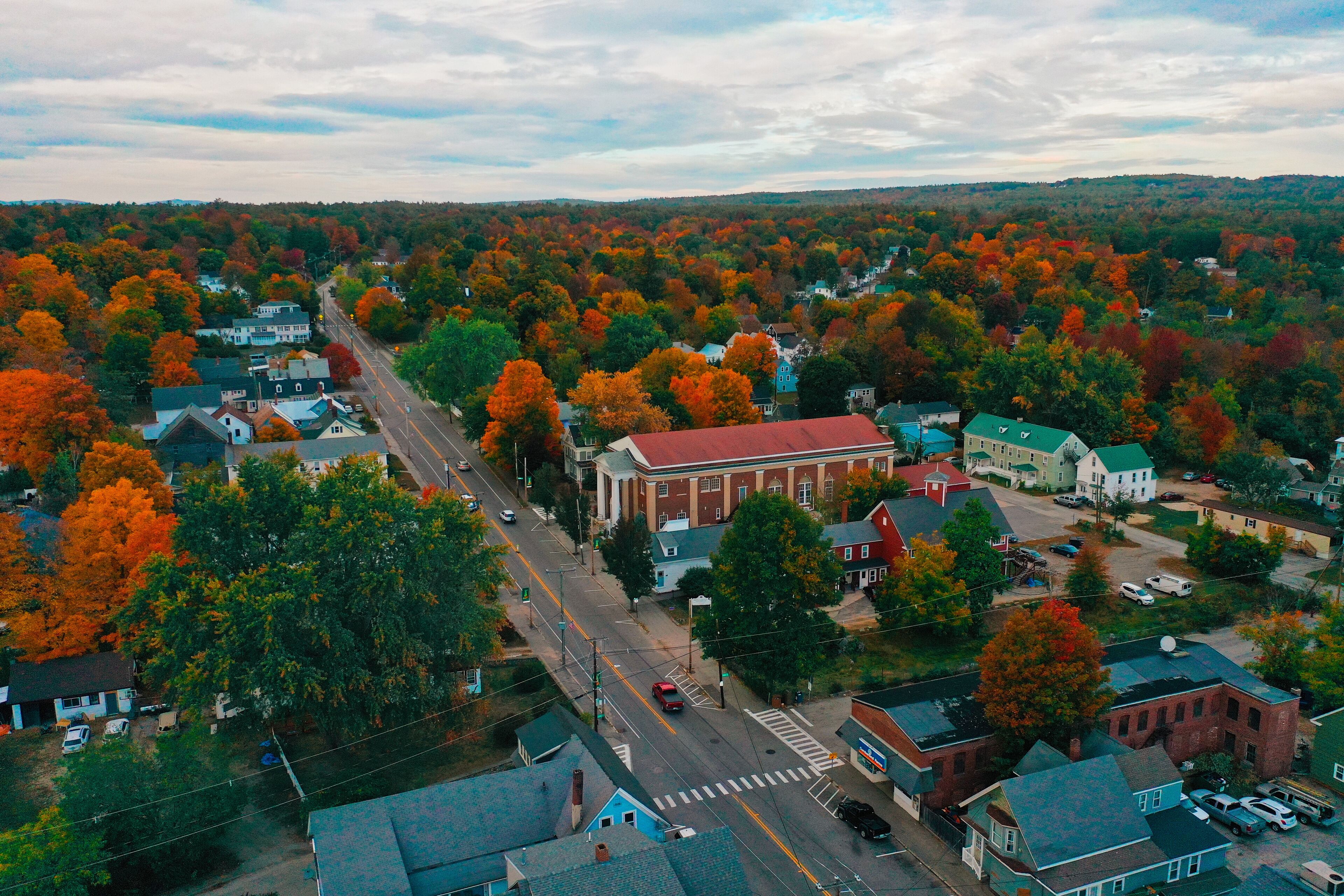 An aerial view of a town with autumn-colored trees, a main road, and various buildings.