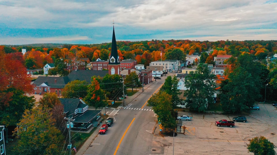 A town with a prominent church steeple, a main street, and autumn-colored trees.