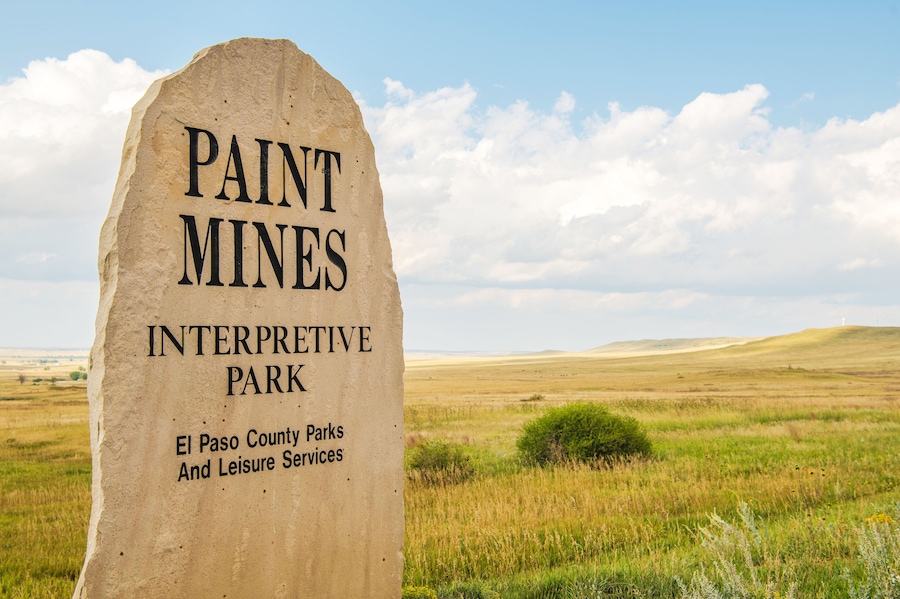 A sign for Paint Mines Interpretive Park with a grassy landscape in the background.