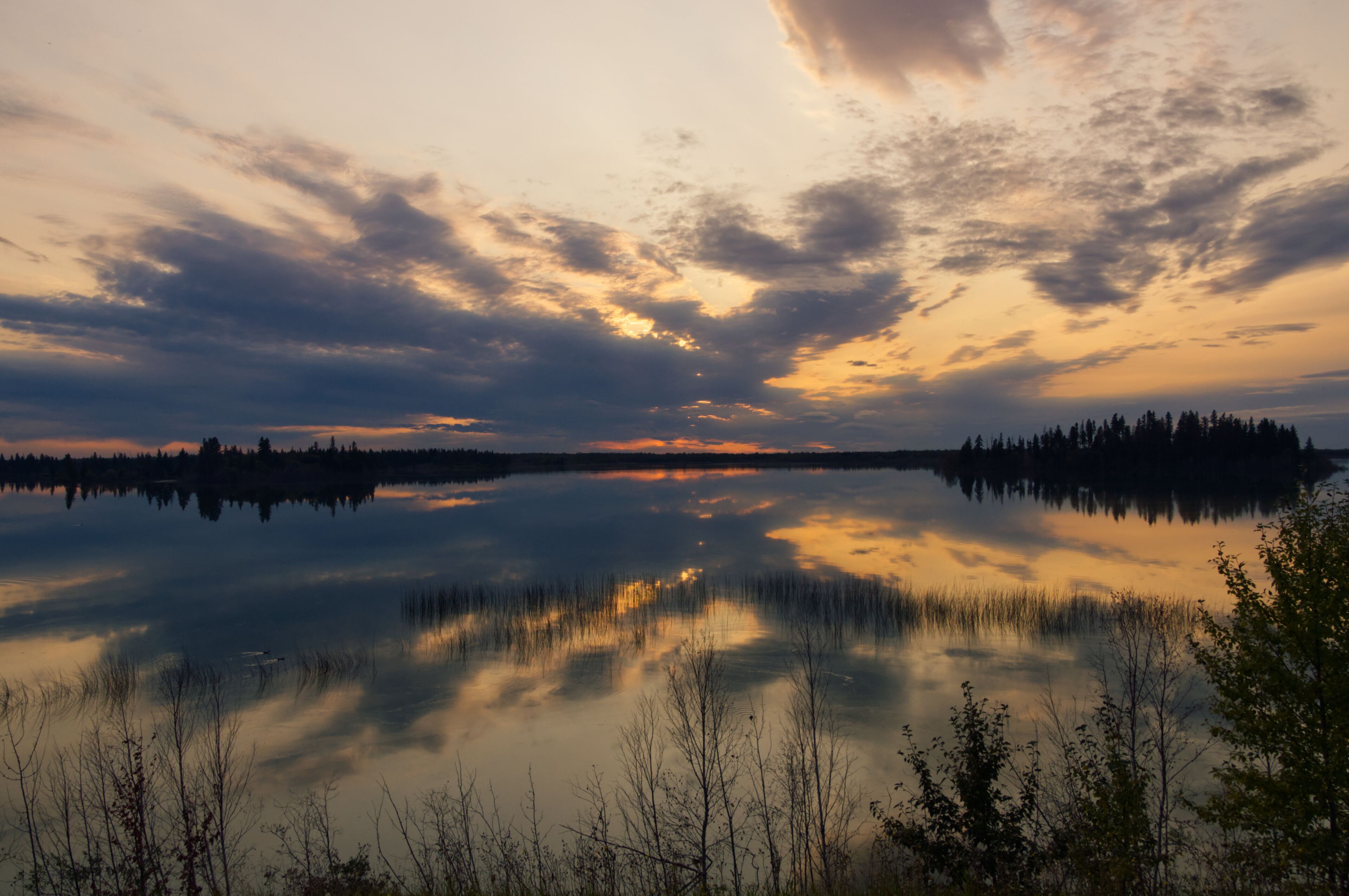 A calm lake at sunset with reflections of trees and sky.