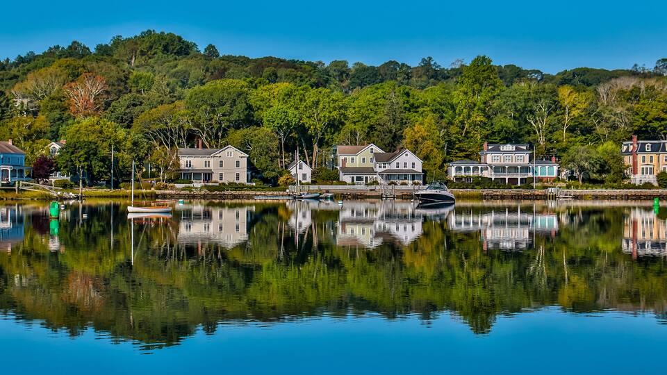 A calm lake with reflections of houses and trees.
