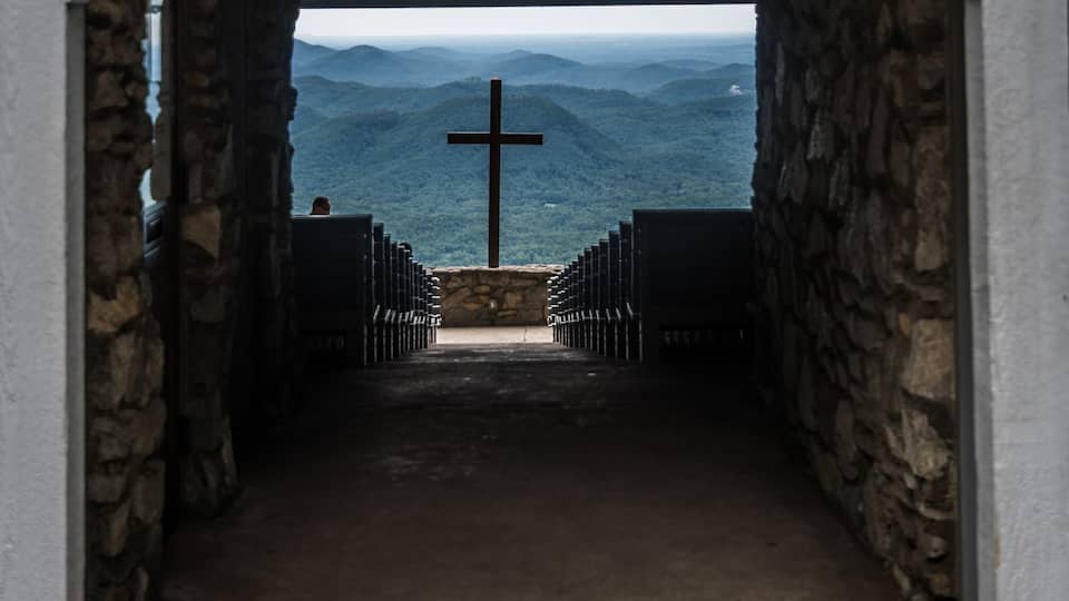 An arched entrance to Camp Greenville with a cross and a view of the mountains.