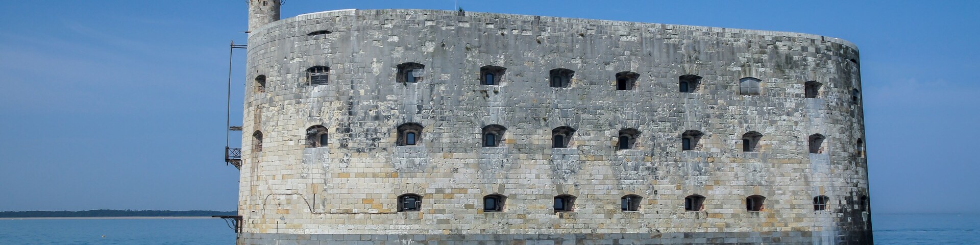Una gran estructura cilíndrica de piedra con varias ventanas, flotando sobre aguas tranquilas bajo un cielo despejado.