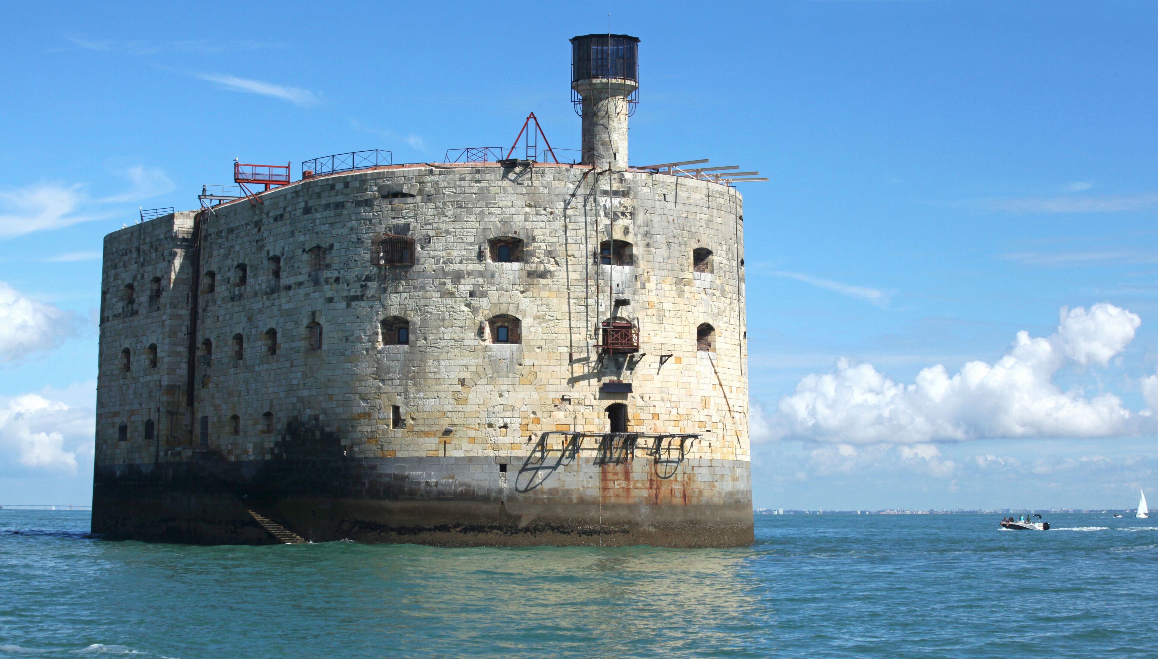 A large, cylindrical stone structure with multiple windows and a central tower, situated in a body of water.