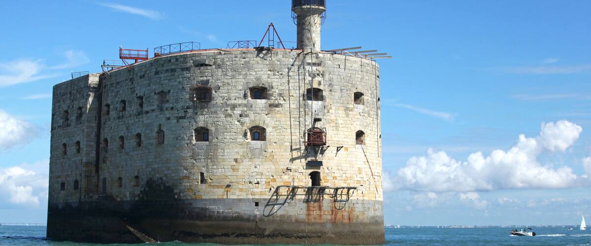 A large, cylindrical stone structure with multiple windows and a central tower, situated in a body of water.