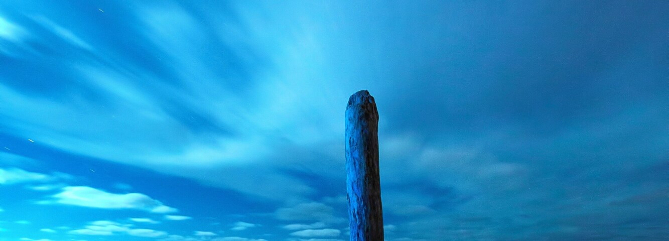 Um poste de madeira em uma paisagem arenosa sob um céu crepuscular.