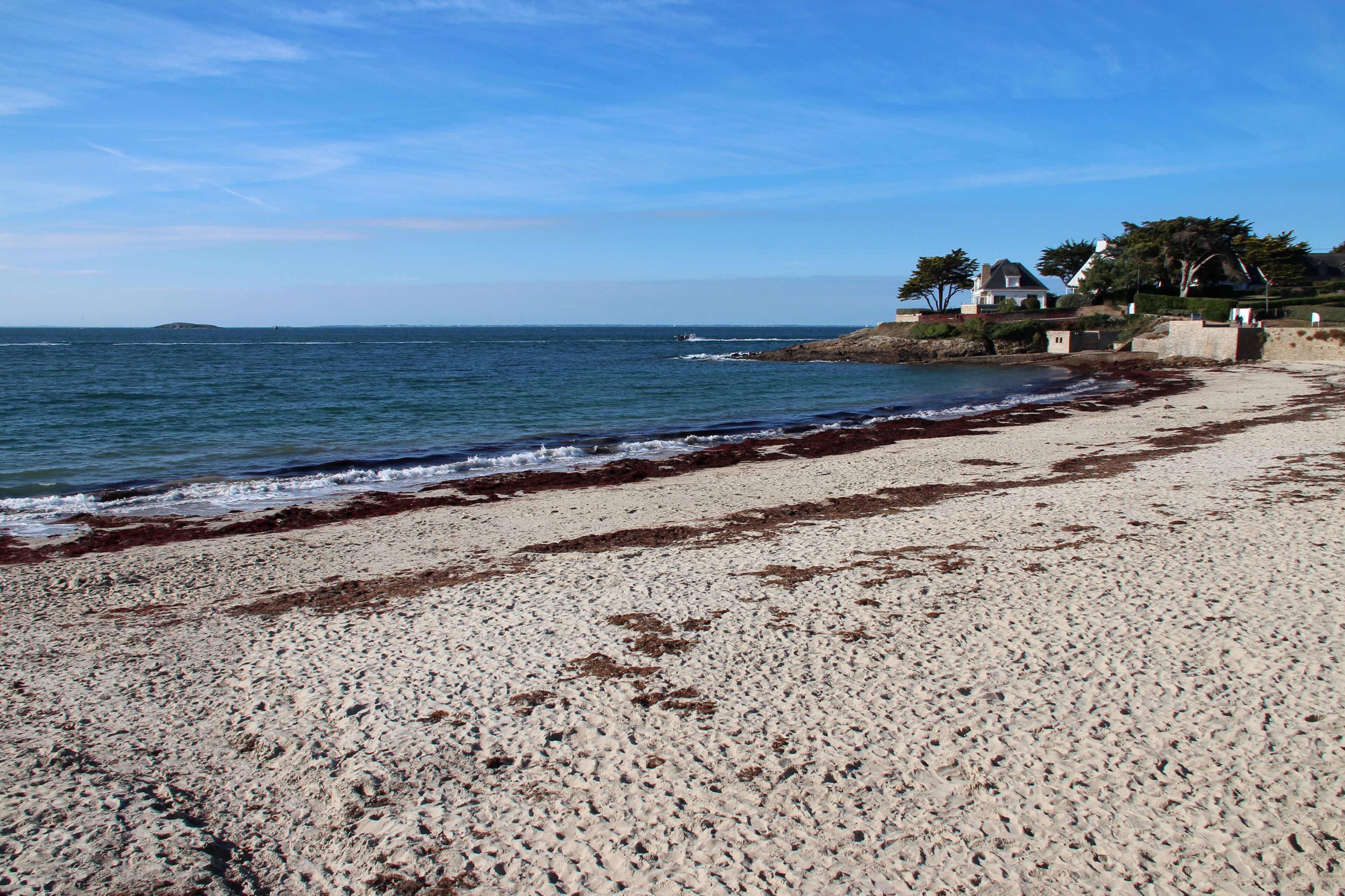 A sandy beach with waves, a clear sky, and houses on a hill.