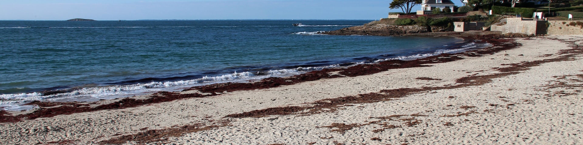 A sandy beach with waves, a clear sky, and houses on a hill.