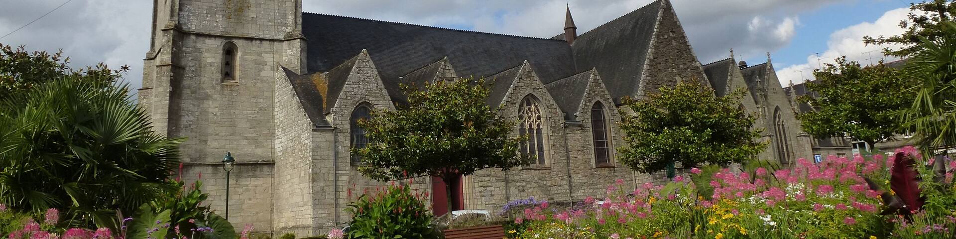 A historic church with a tall spire and a clock tower, surrounded by a vibrant garden with various flowers.