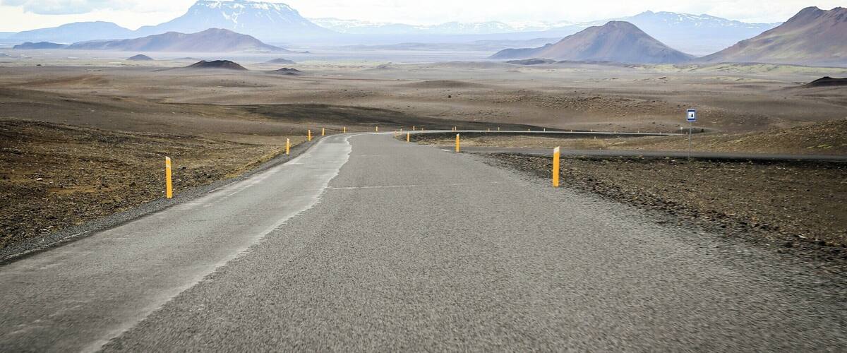 A road in a barren landscape with mountains in the distance.
