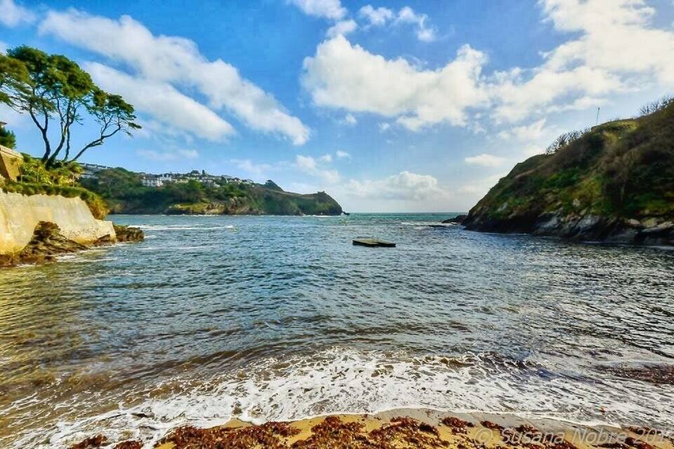 Paisagem costeira com águas claras, uma praia de areia e falésias rochosas.