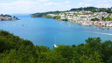 A coastal town with a harbor filled with boats, surrounded by lush greenery and historic buildings.