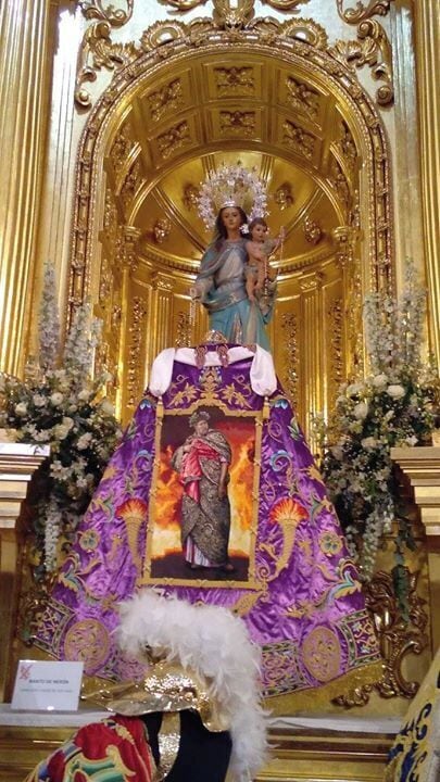 A religious statue with a child, surrounded by ornate golden decorations and floral arrangements.