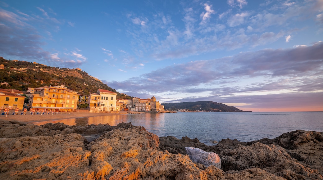 A coastal town with buildings on a hillside, rocky shoreline, and calm sea.