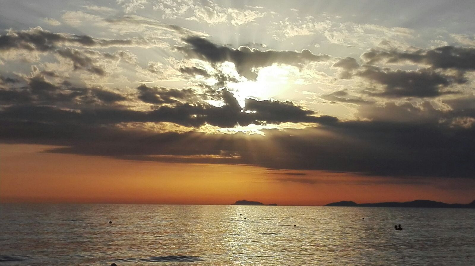 Un atardecer sobre un mar tranquilo con nubes dispersas y tierras lejanas.