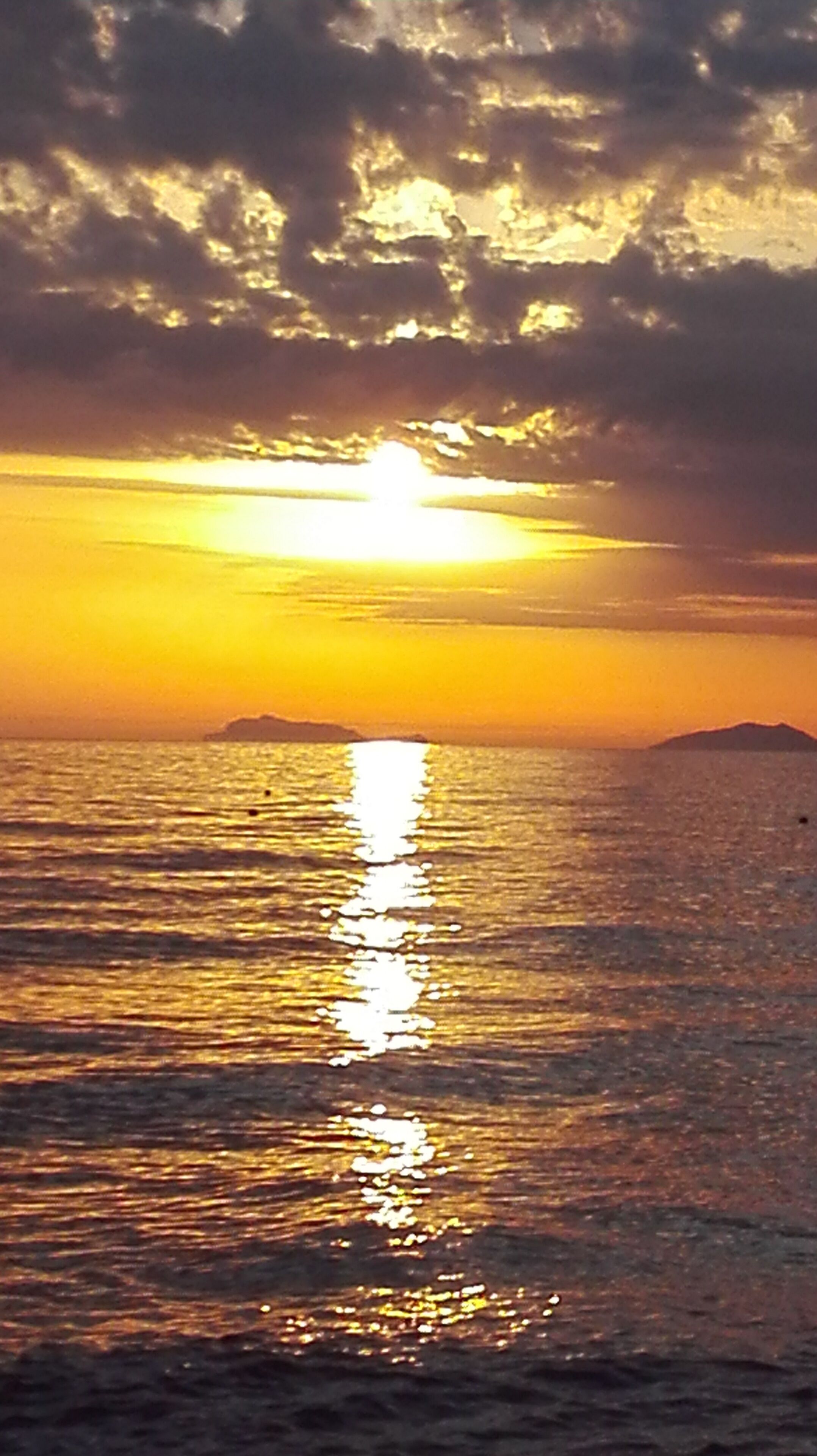 Un atardecer sobre un mar tranquilo, con el reflejo claro del sol en el agua.