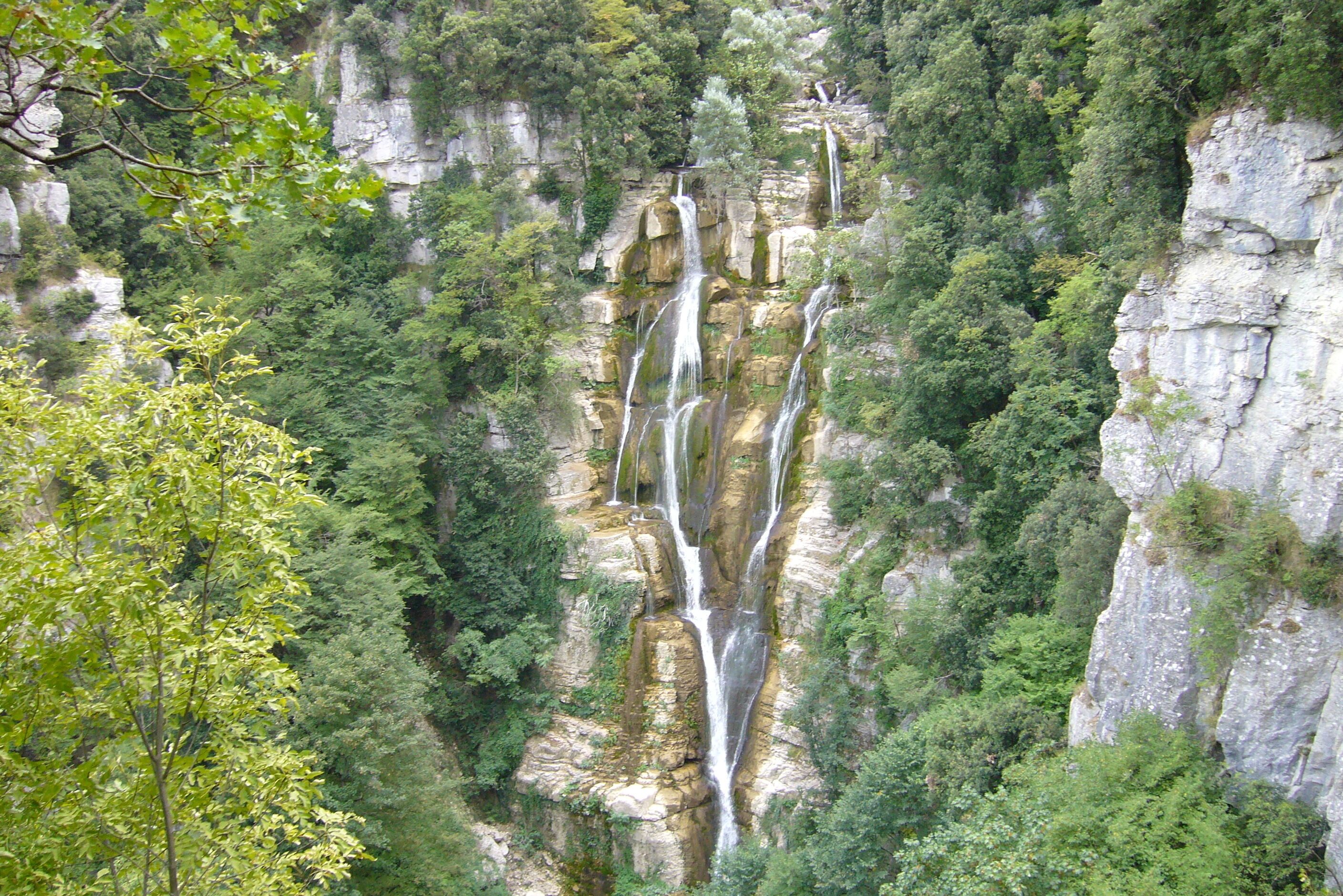 A multi-tiered waterfall cascading down a rocky cliff surrounded by dense greenery.