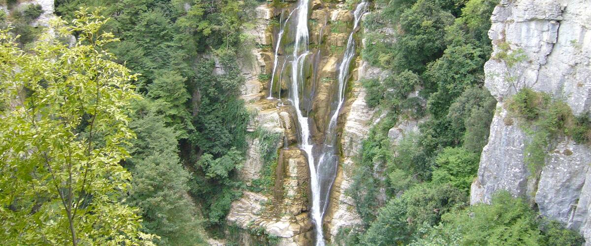 A multi-tiered waterfall cascading down a rocky cliff surrounded by dense greenery.