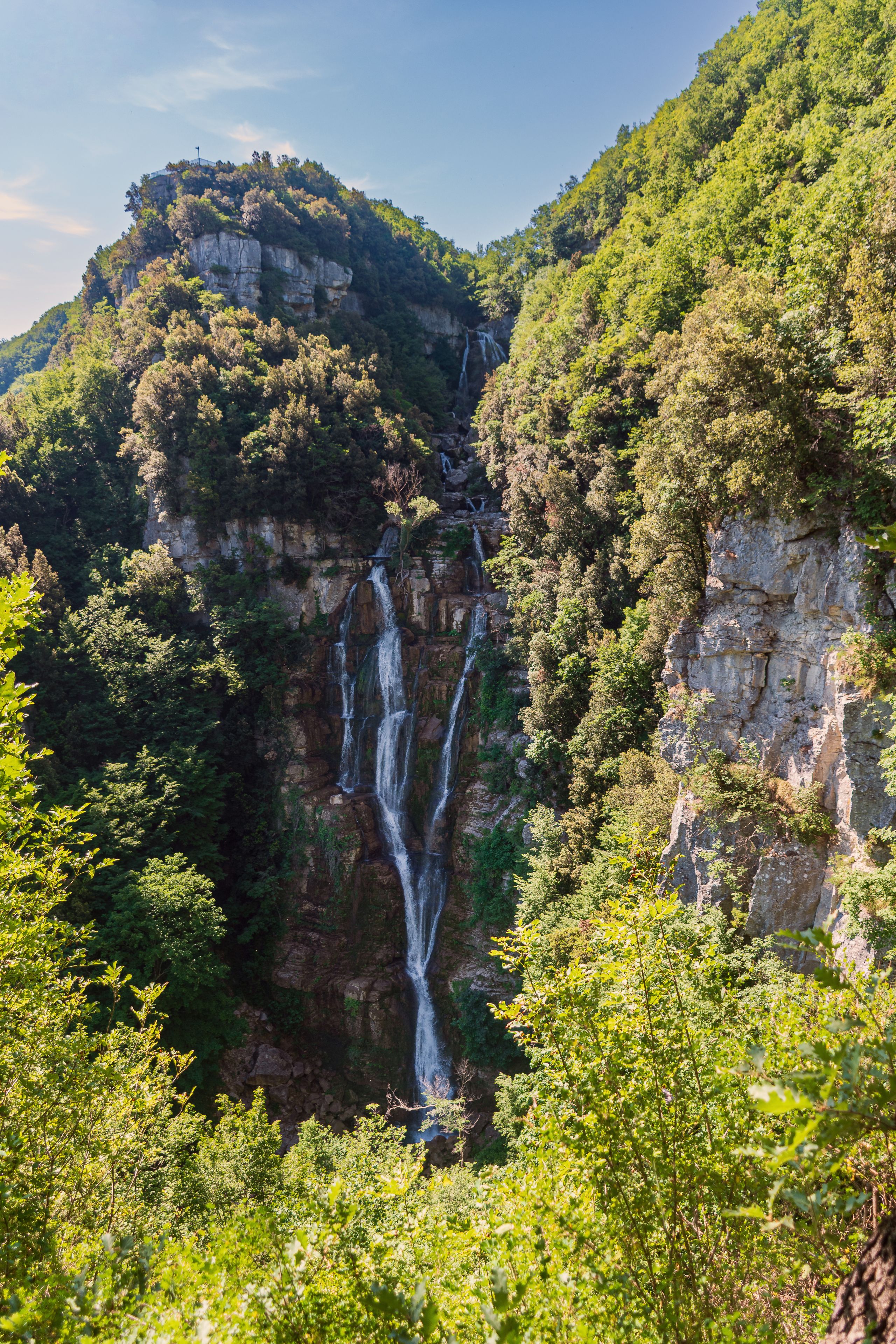Een waterval stort neer over een rotswand, omringd door weelderige vegetatie.