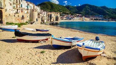 A coastal town with boats on the beach, buildings, and mountains in the background.