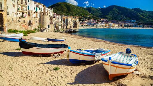 Una cittadina costiera con barche sulla spiaggia, edifici storici e una montagna sullo sfondo.
