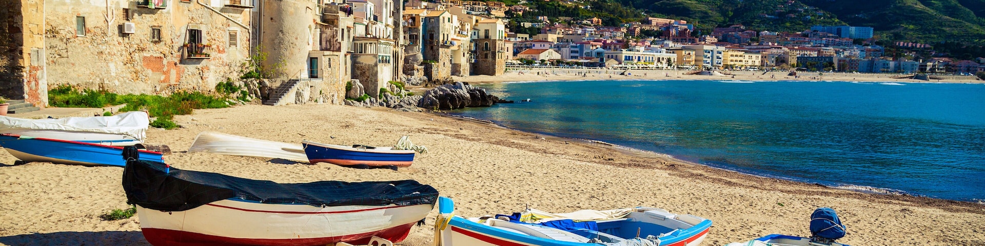 Un pueblo costero con barcos en la playa, edificios históricos y una montaña al fondo.