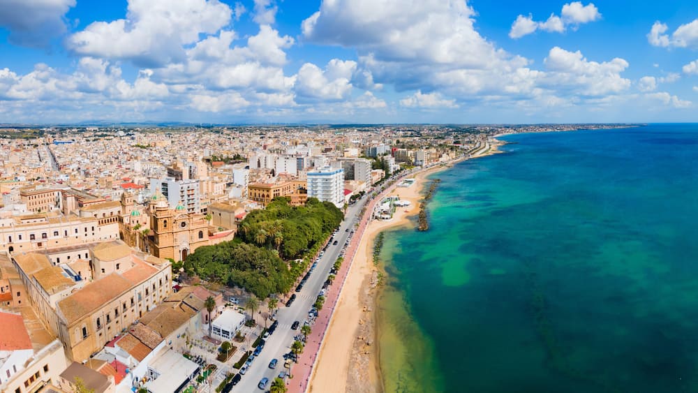 Un paysage urbain côtier avec une plage bien visible, des bâtiments urbains denses et un ciel bleu dégagé.