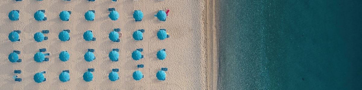 Aerial view of a well sorted lido with blue parasols and sunbeds at sunrise along the coastline in Calabria, Italy.