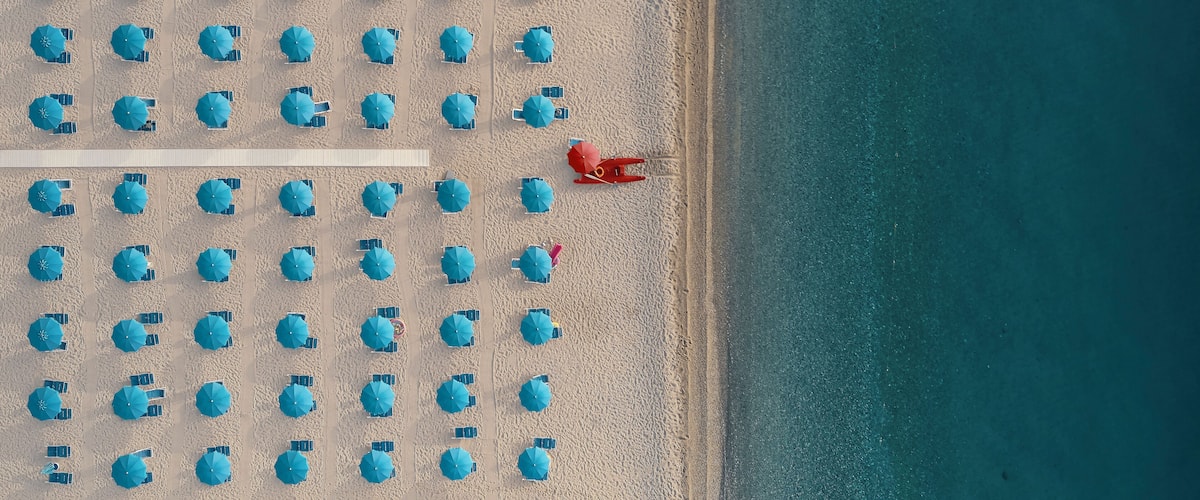 Aerial view of a well sorted lido with blue parasols and sunbeds at sunrise along the coastline in Calabria, Italy.