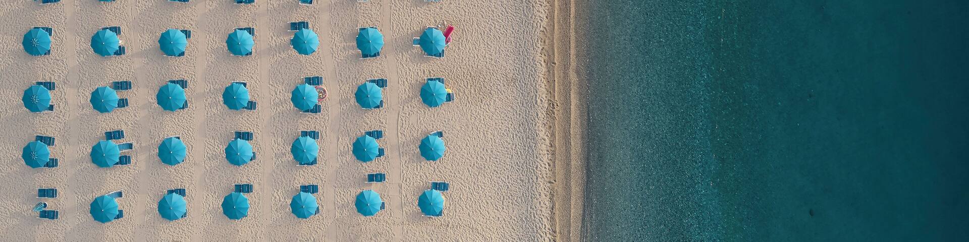 Aerial view of a well sorted lido with blue parasols and sunbeds at sunrise along the coastline in Calabria, Italy.