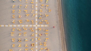 Luftaufnahme eines Strandes mit Liegestühlen und einem Rettungsturm.