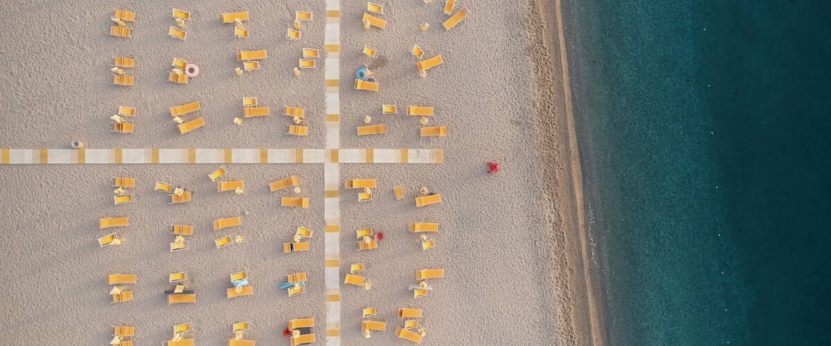 An aerial view of a beach with rows of sun loungers and a lifeguard tower.
