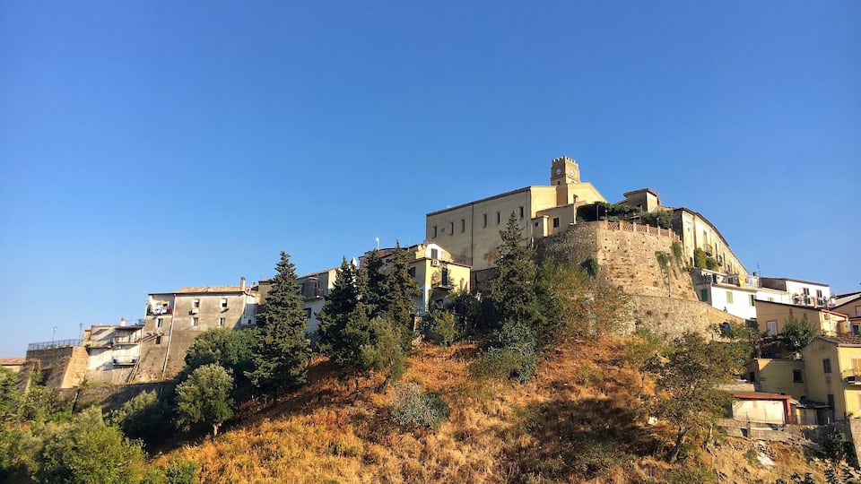 A historic castle on a hill with surrounding buildings and trees.