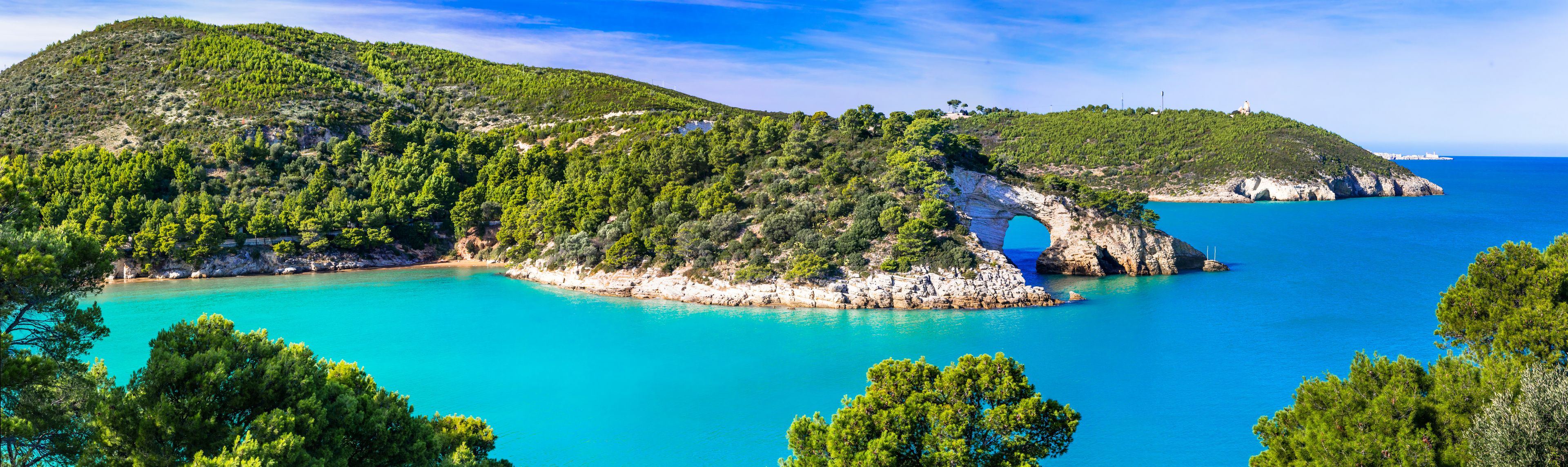 Un paisaje costero con una formación rocosa destacada, un mar turquesa cristalino y una vegetación verde exuberante.