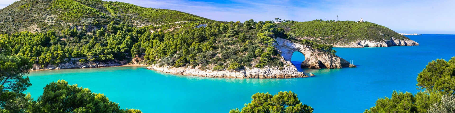 Un paisaje costero con una formación rocosa destacada, un mar turquesa cristalino y una vegetación verde exuberante.