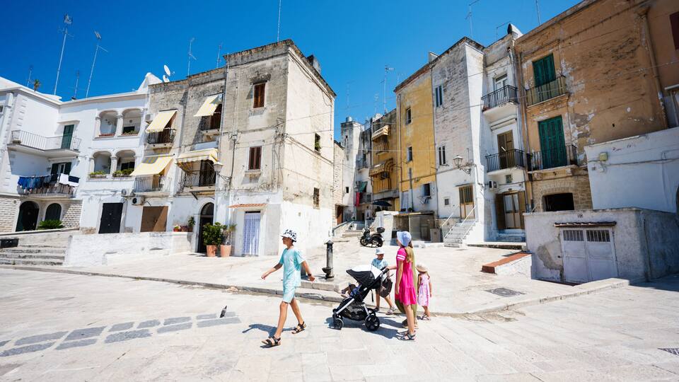 A pedestrian street with historic buildings, a stroller, and a clear blue sky.